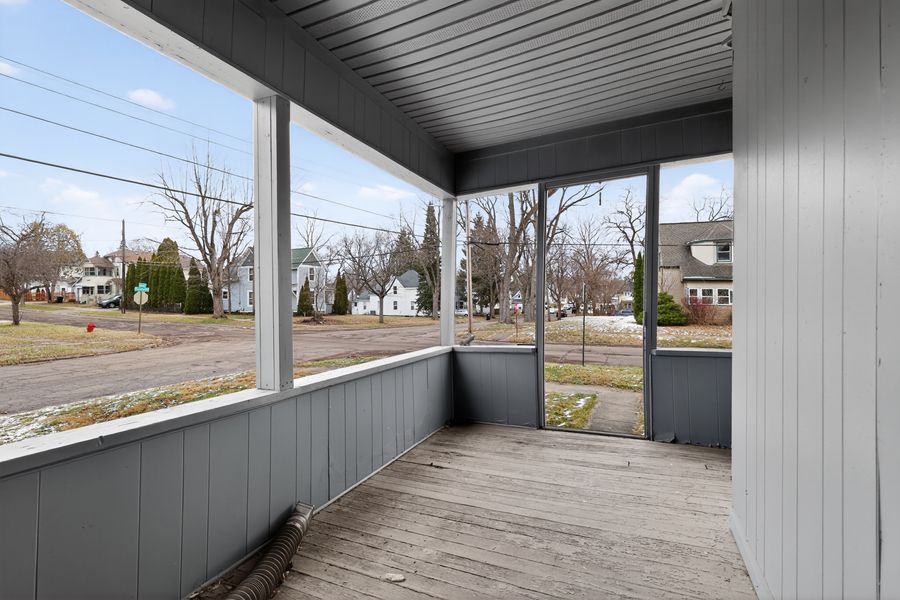 Screened porch with gray wood paneling, wooden deck flooring, and views of a quiet residential neighborhood.