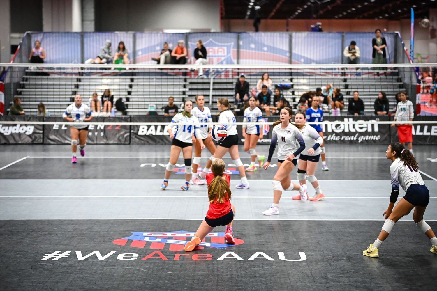 Young athletes compete in an AAU volleyball tournament on an indoor court with #WeAreAAU branding on the floor.