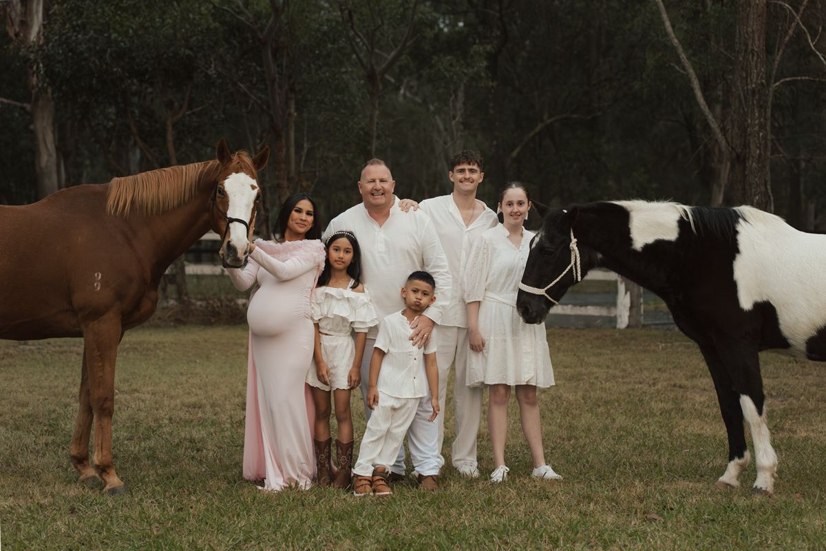 Family maternity photo with two horses outdoors, parents and three children dressed in white and pink photoshoot with horses in sydney
