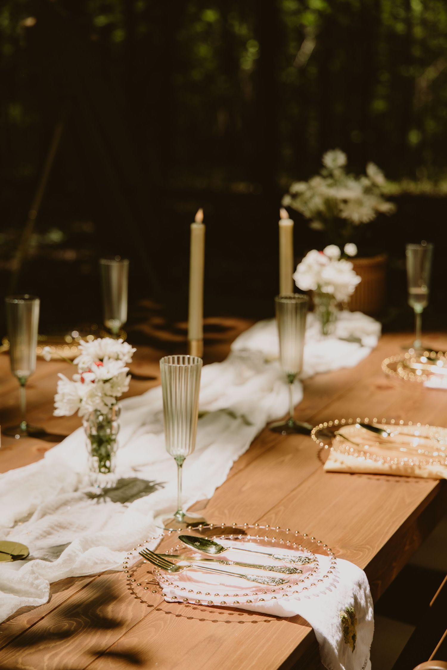 Elegant outdoor wedding table setting with candles, floral arrangements, and a white runner on a wooden table.