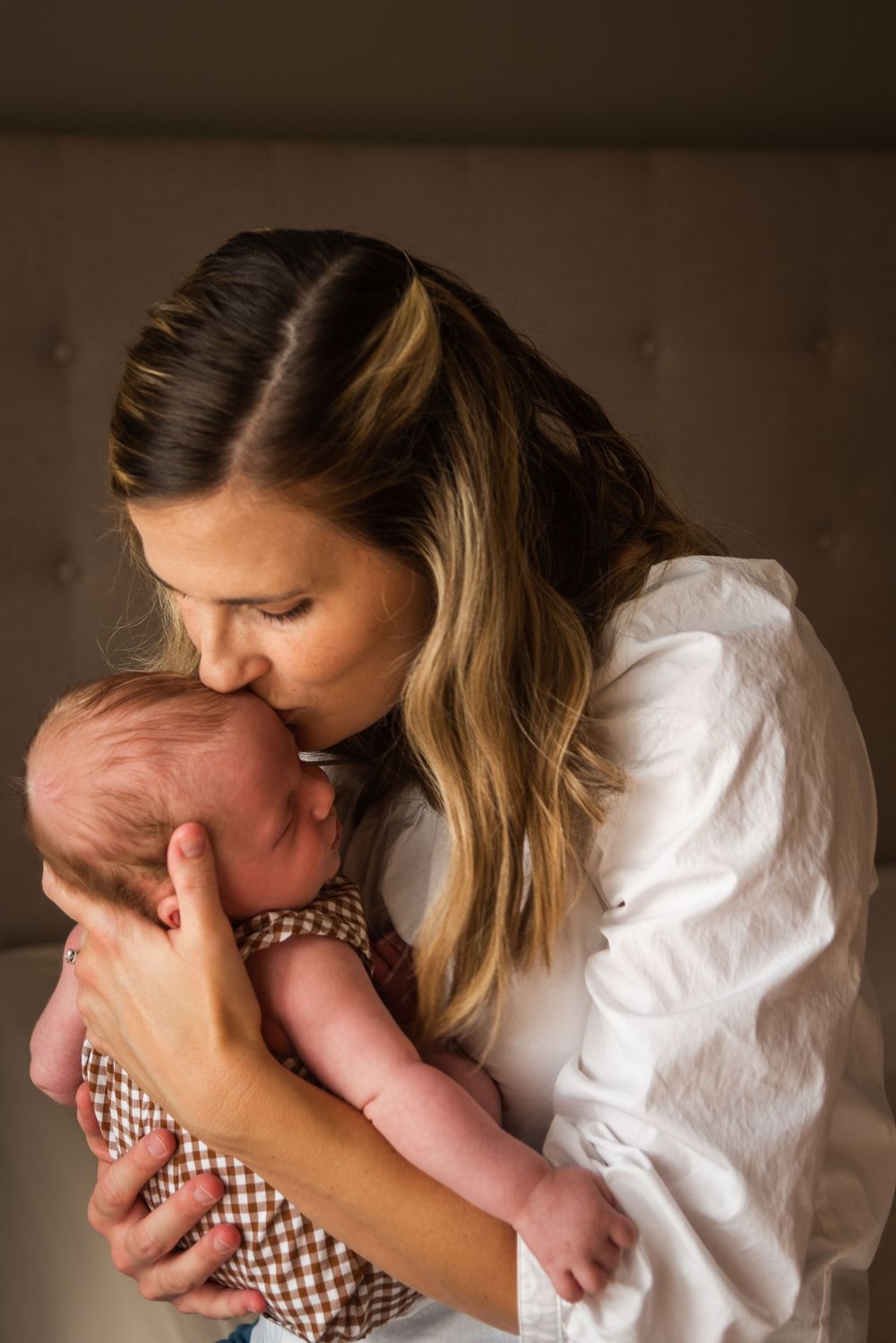 A mother tenderly kisses her newborn baby while cradling them gently in her arms.