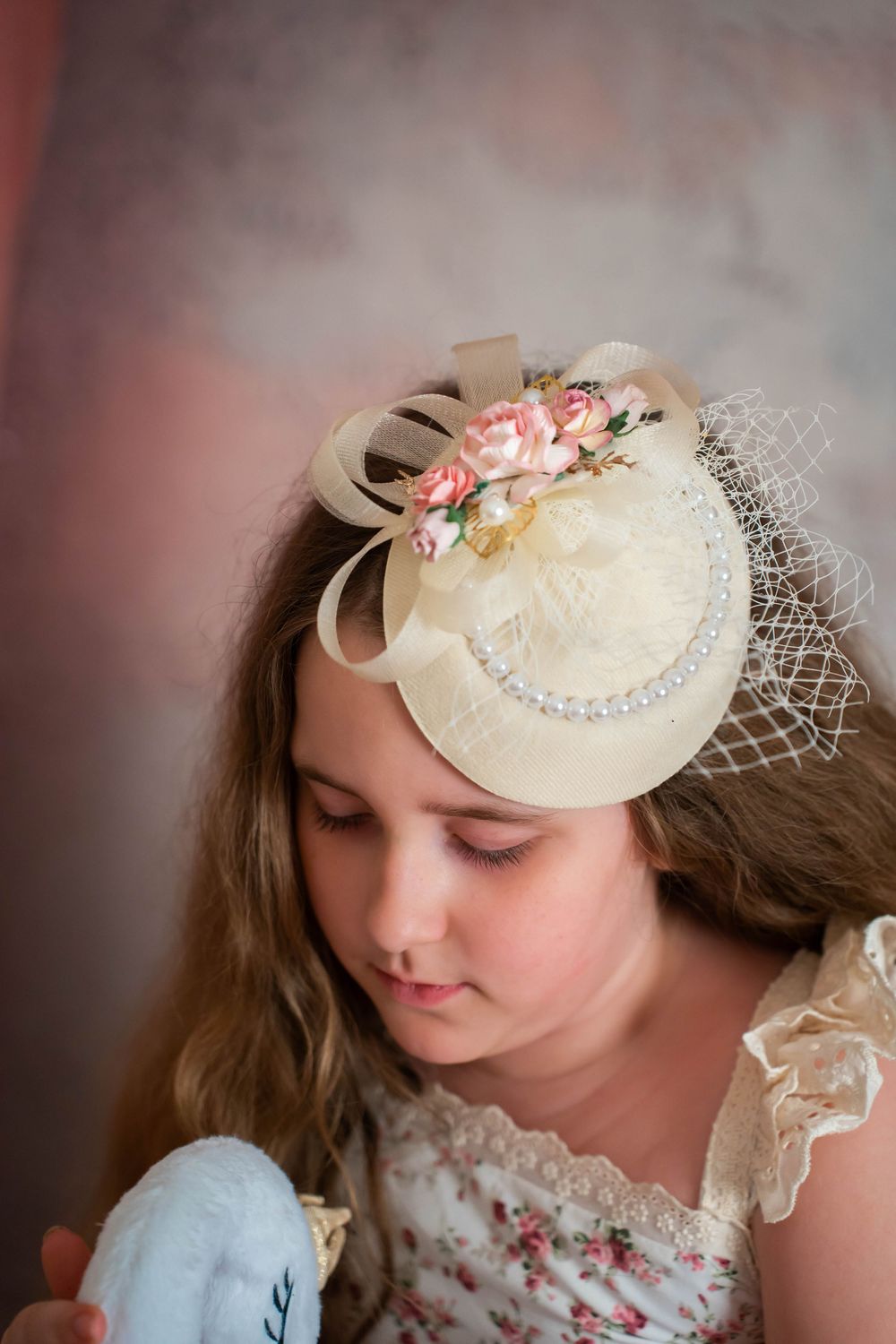 Young girl wearing an elegant cream fascinator hat with flowers and pearl trim.