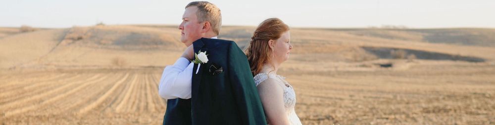 Bride and groom standing back-to-back in a golden wheat field on their wedding day.