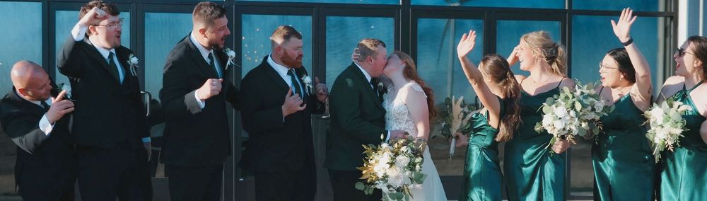 Wedding party in emerald green dresses and suits celebrate as couple shares first kiss at altar.