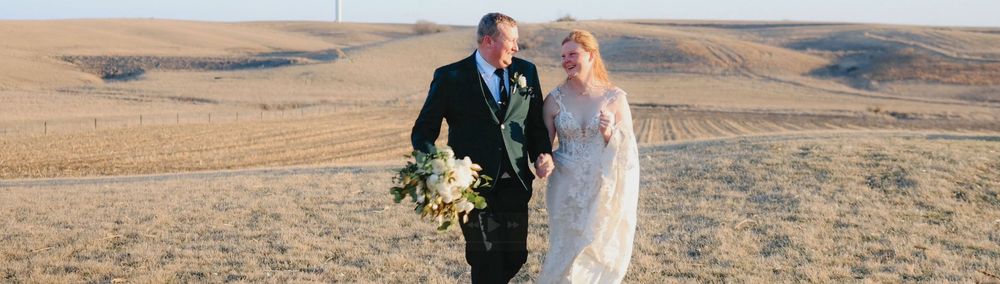 A newlywed couple walks hand in hand through a stunning open field on their wedding day.