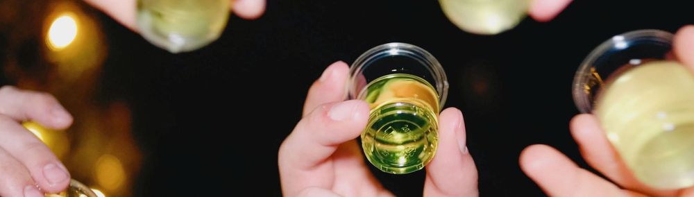 Friends raising shot glasses filled with green liquid for a celebratory toast at a party.