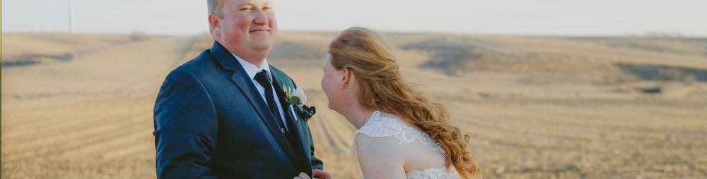A bride and groom share a romantic moment on their wedding day in a vast golden prairie landscape.