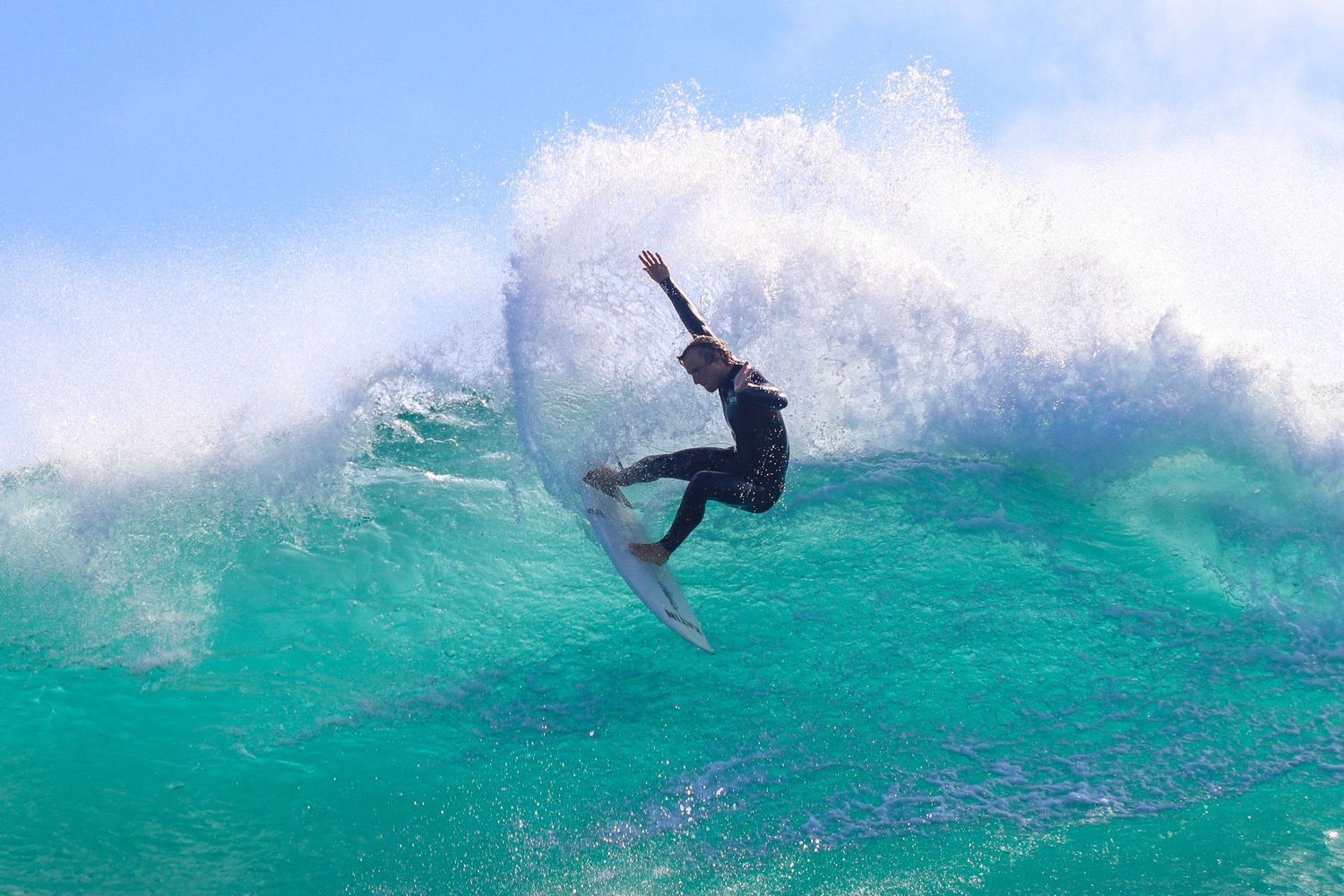 Trestles surf photography of a male surfer in a wetsuit carving a large, bright turquoise wave.