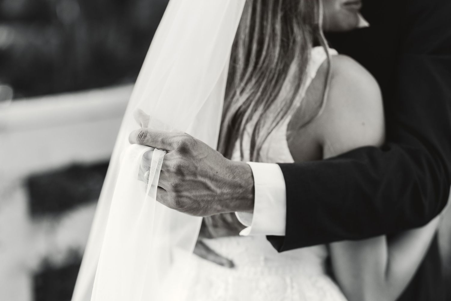 Black and white photo of bride and groom embracing, showcasing wedding dress, veil, and groom suit at elegant ceremony.