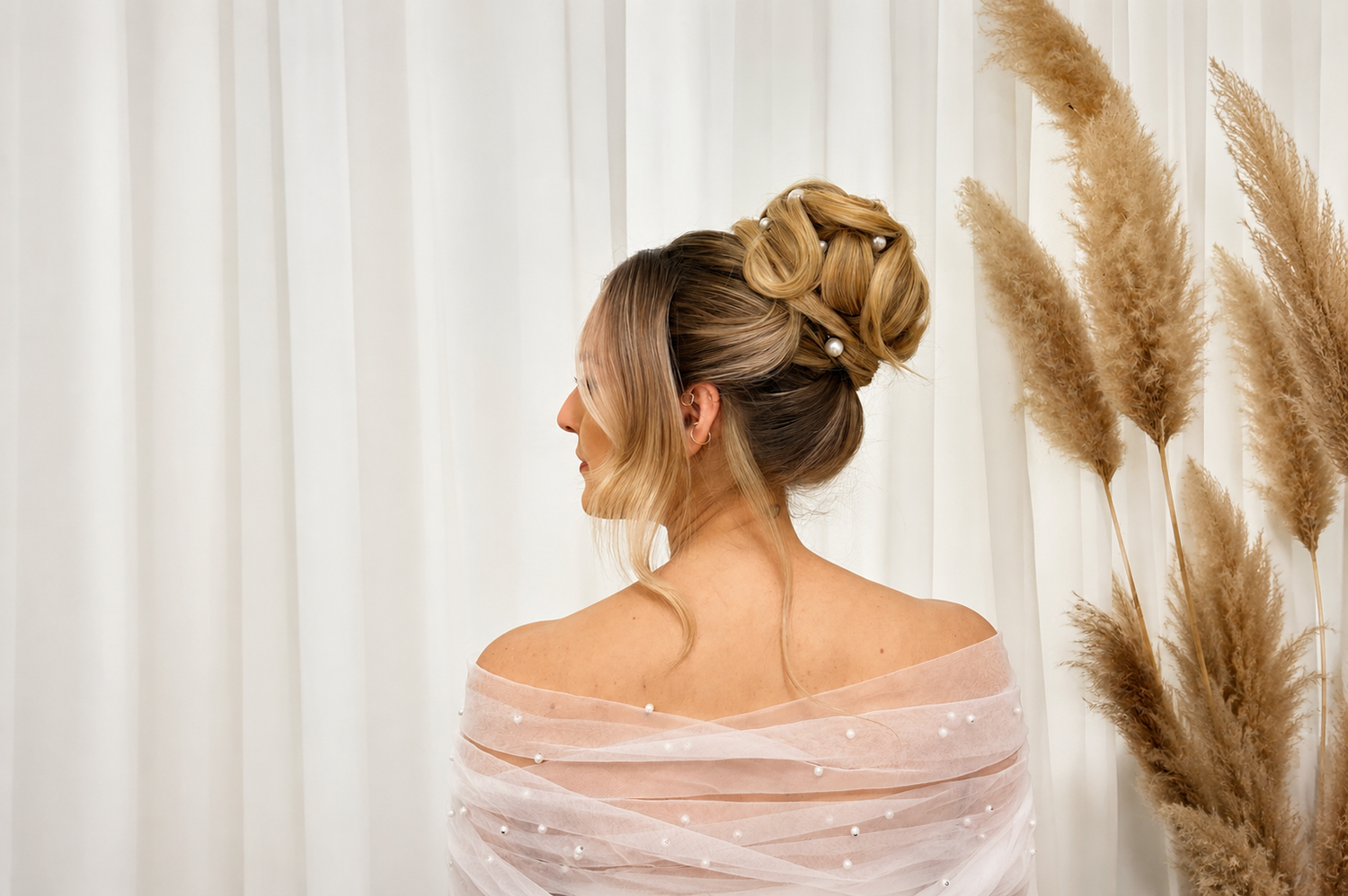 Bride with half-up blonde wavy hairstyle adorned with white flowers, wearing a lace backless wedding gown.