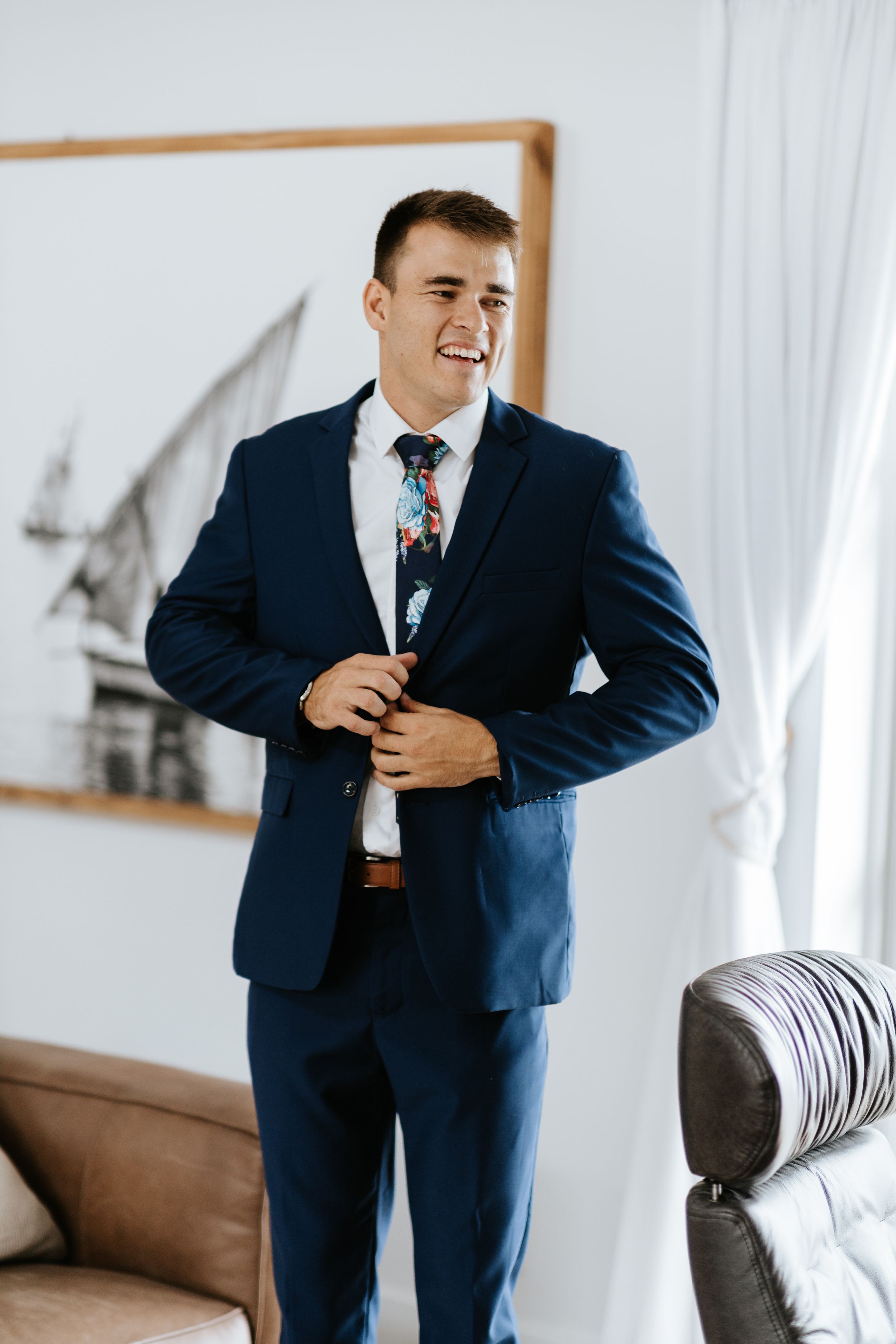 Person in navy blue suit with floral tie smiling in bright interior setting.