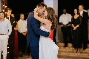 Couple sharing their first dance at an indoor wedding reception with string lights and guests watching.