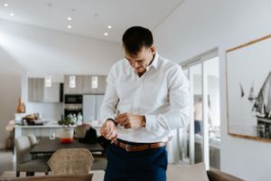 Person in white dress shirt adjusting cuffs while getting ready in modern room.