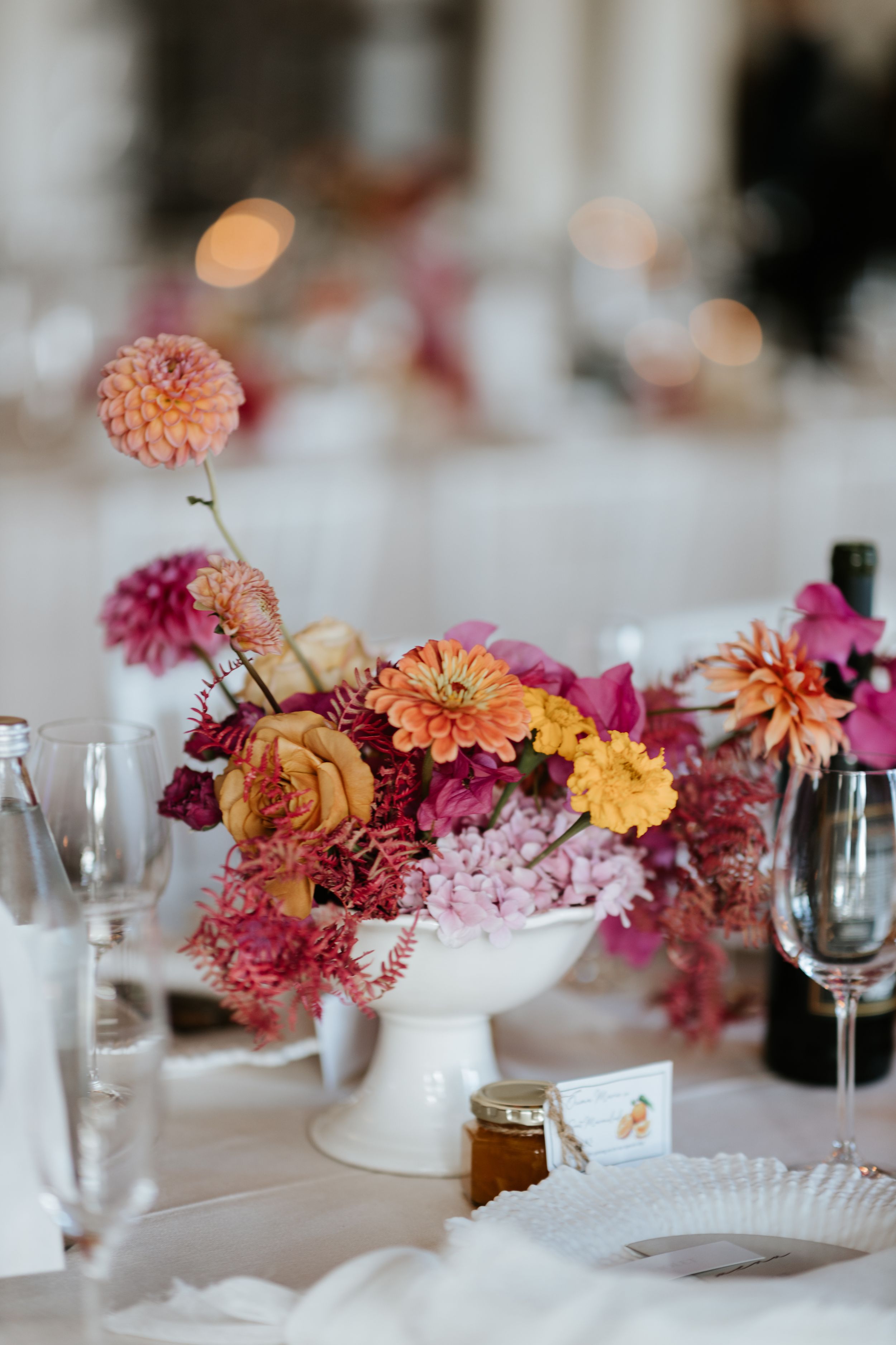 Elegant floral centerpiece with pink and orange dahlias in white vase on wedding reception table.