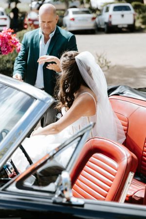 Classic car wedding scene with vintage coral convertible and flowing veil.