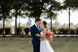 Romantic moment between newlyweds in a garden setting with coral bouquet and navy suit.