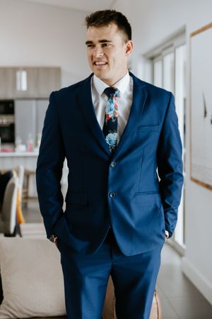 Person wearing tailored navy blue suit with patterned tie standing in modern room.