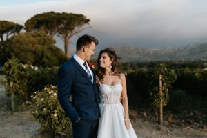 Romantic sunset portrait of couple in wedding attire against vineyard backdrop.