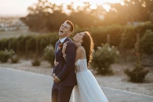 Joyful wedding couple laughing together during golden hour photoshoot.