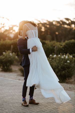 Playful wedding couple dancing outdoors with bride's dress flowing in the wind.