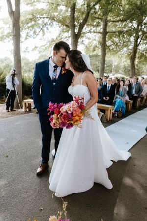 A couple shares an intimate moment during their wedding ceremony holding a vibrant pink bouquet.