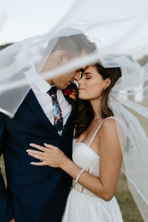 Romantic portrait under flowing veil with couple in classic wedding attire.