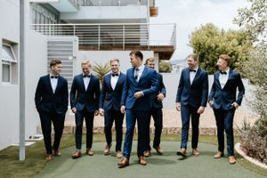 Groomsmen in matching navy suits and bow ties walking together outdoors.