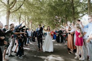 Wedding guests line a tree-lined path throwing confetti during the ceremony exit.