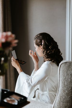 Getting ready scene with white robe and makeup application in morning light.