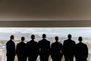 Silhouette of groomsmen standing against panoramic window view.
