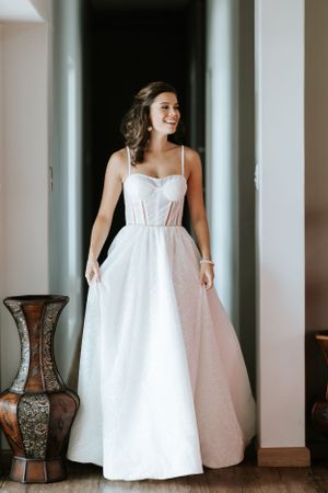 Full length view of white structured wedding gown with corset detail beside decorative vase.