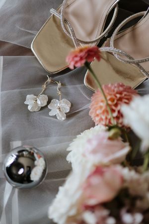 Wedding accessories including delicate floral earrings and pink flowers arranged with sheer fabric and jewelry.