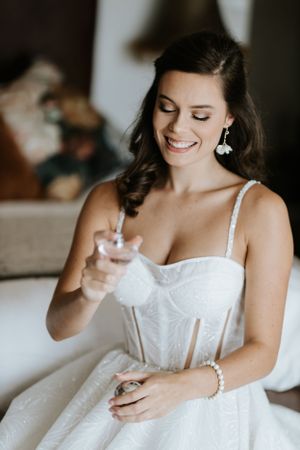 Close up of bride in white structured wedding dress holding perfume bottle.
