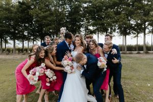 Wedding party shares a fun group moment outdoors with bridesmaids in coral dresses and groomsmen in navy suits.