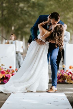A romantic dip kiss during a wedding ceremony surrounded by floral decorations.
