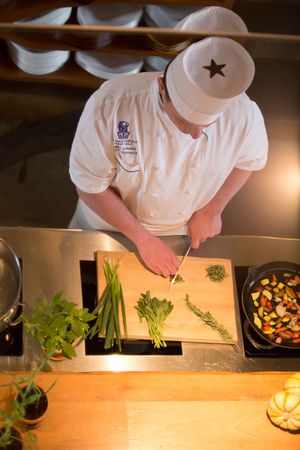 Overhead view of chef chopping fresh herbs including chives and rosemary on cutting board.