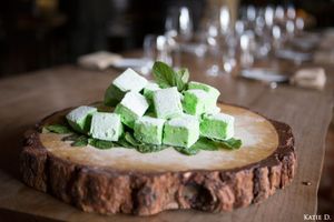 Green mint marshmallow cubes piled on a rustic wooden slice with fresh mint leaves.