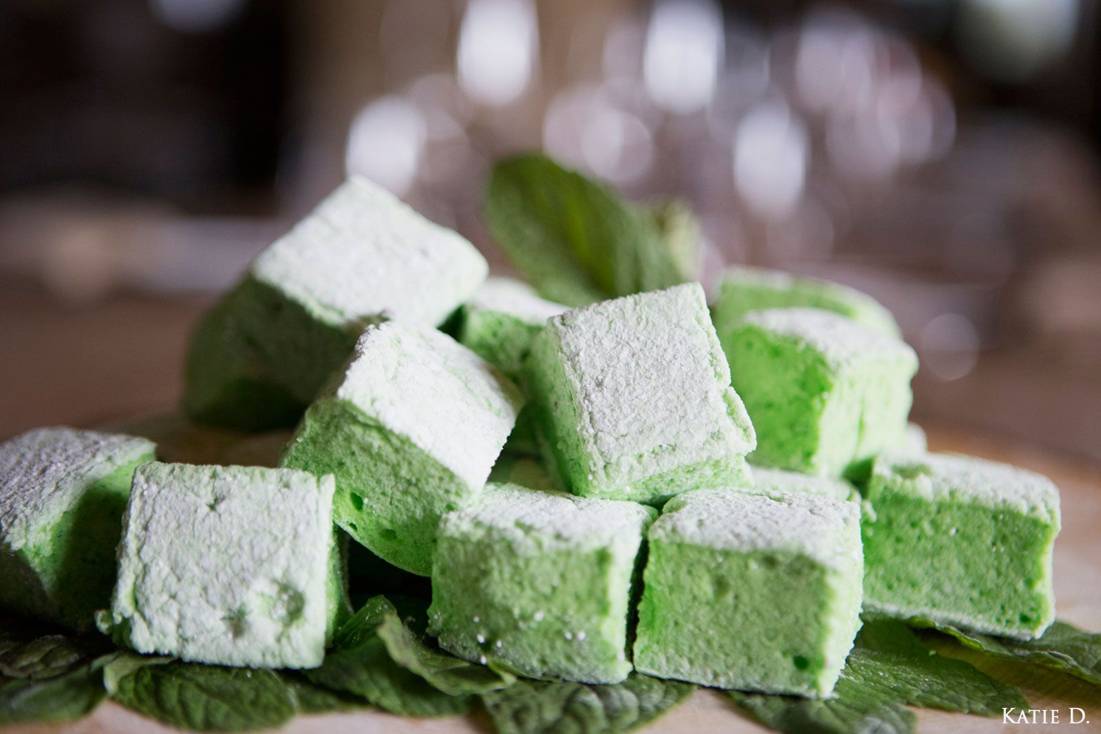 Homemade green mint marshmallows stacked on a plate with fresh basil leaves.
