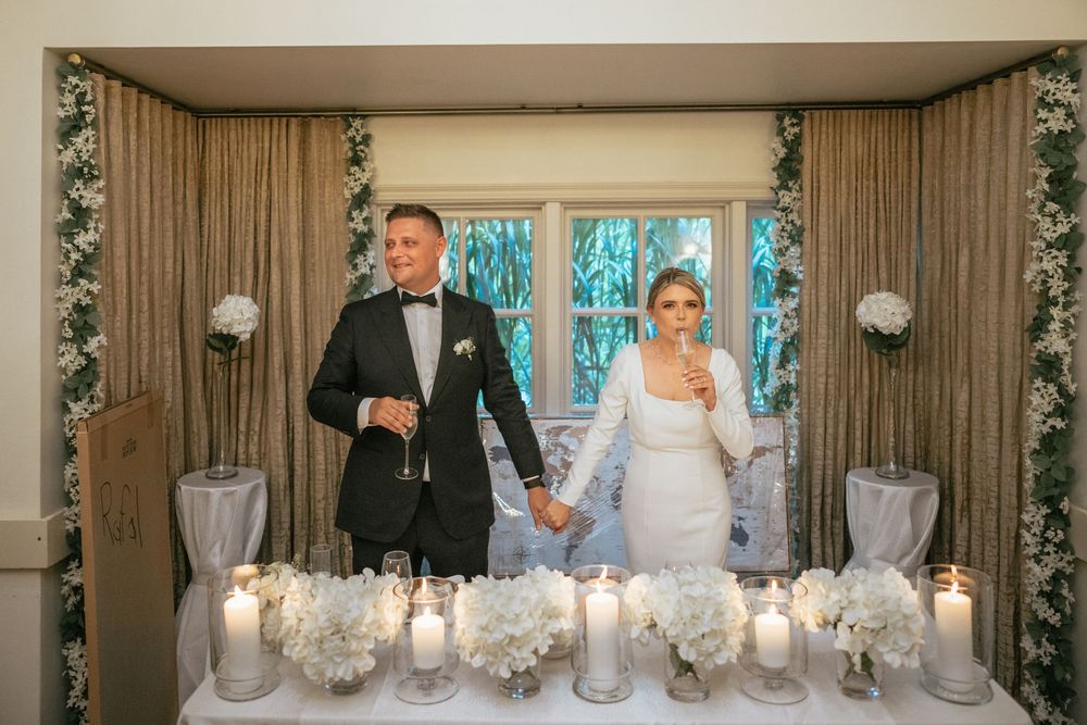 Bride and groom holding hands at elegant wedding altar adorned with white flowers and candles.