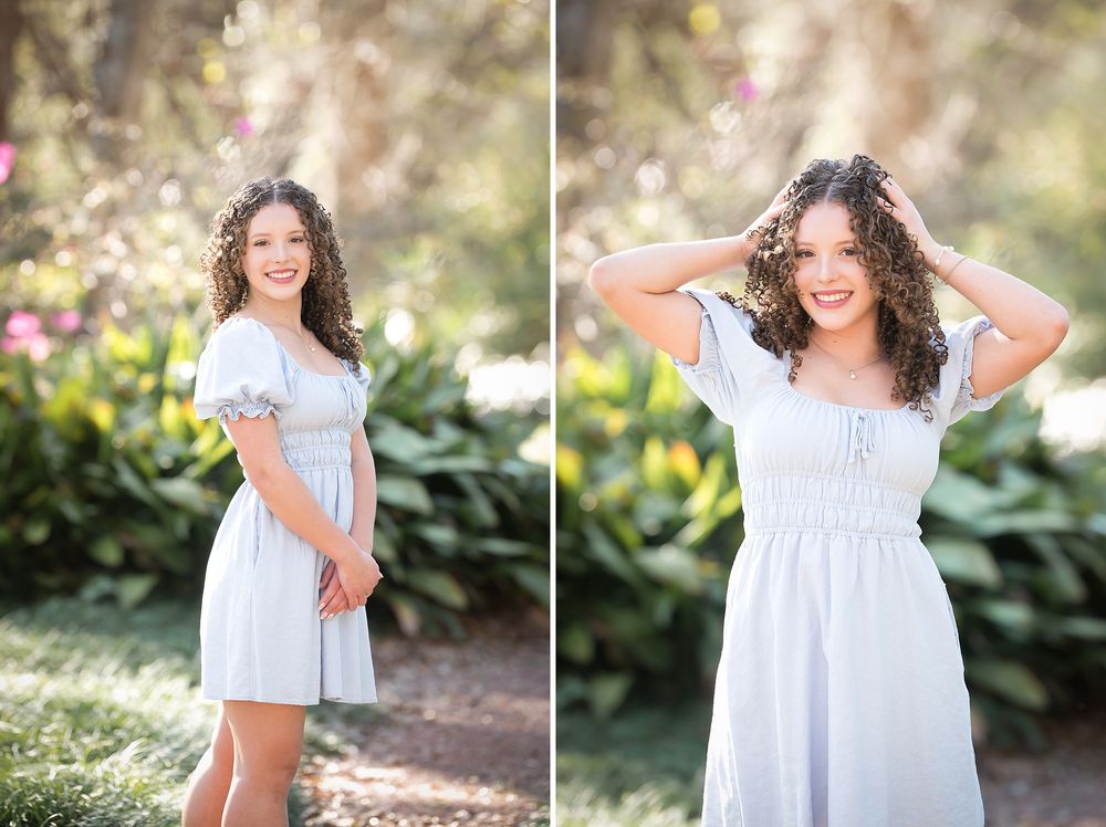 Teen girl in light blue dress poses in a garden with lush greenery and soft pink blooms in the background.