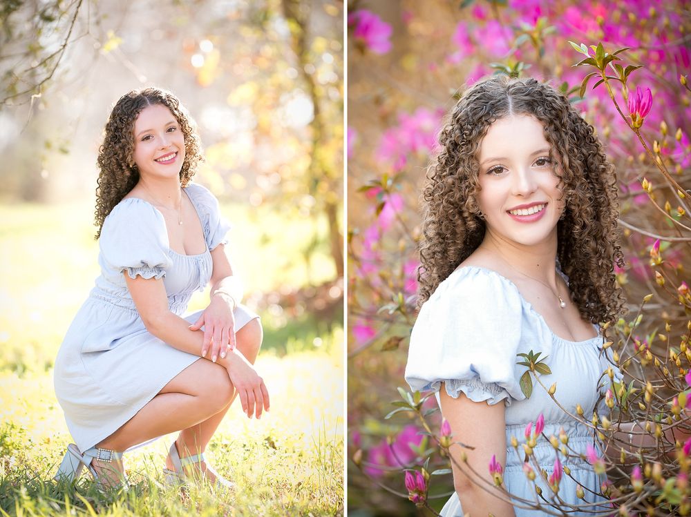 Smiling teen girl with curly hair poses in a light blue dress outdoors among spring flowers and trees.