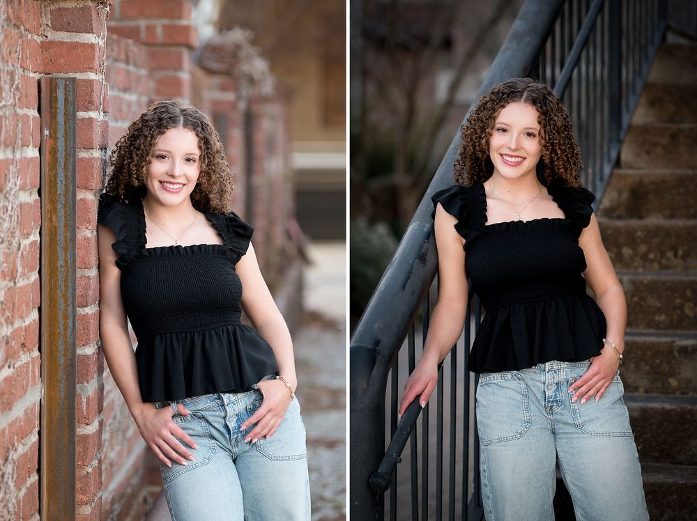 Smiling teen girl with curly hair poses in a black ruffled top and jeans near brick wall and stairs.