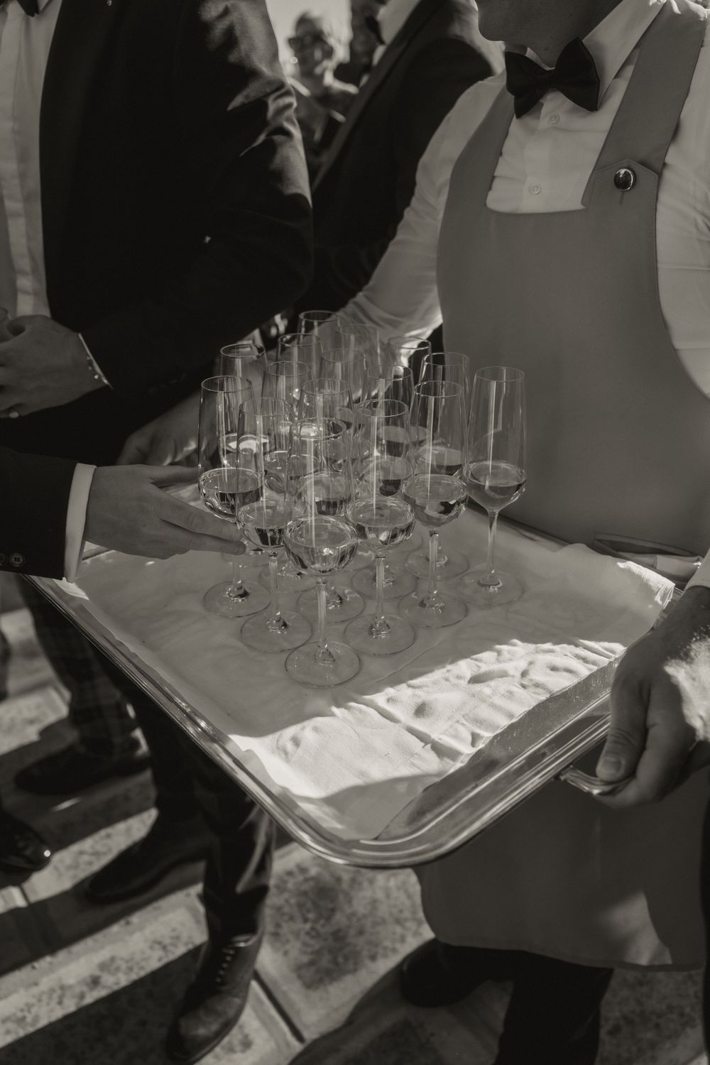 Black and white photo of waiter holding tray of champagne flutes at elegant wedding reception.