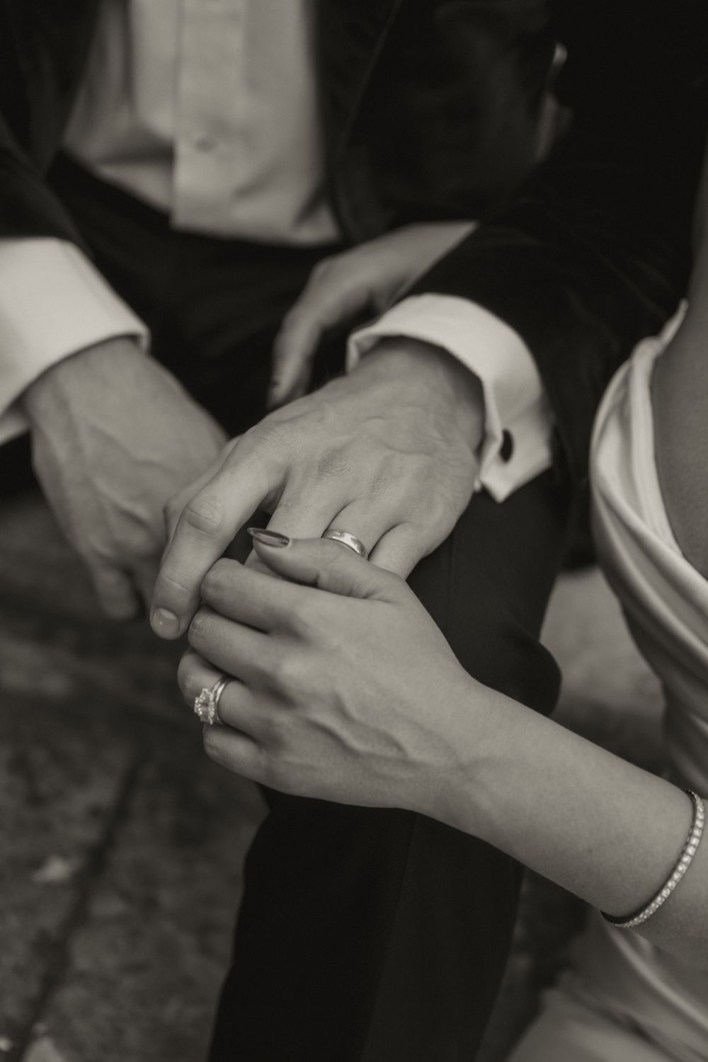 Black and white close-up of newlyweds holding hands showing wedding rings and diamond engagement ring.