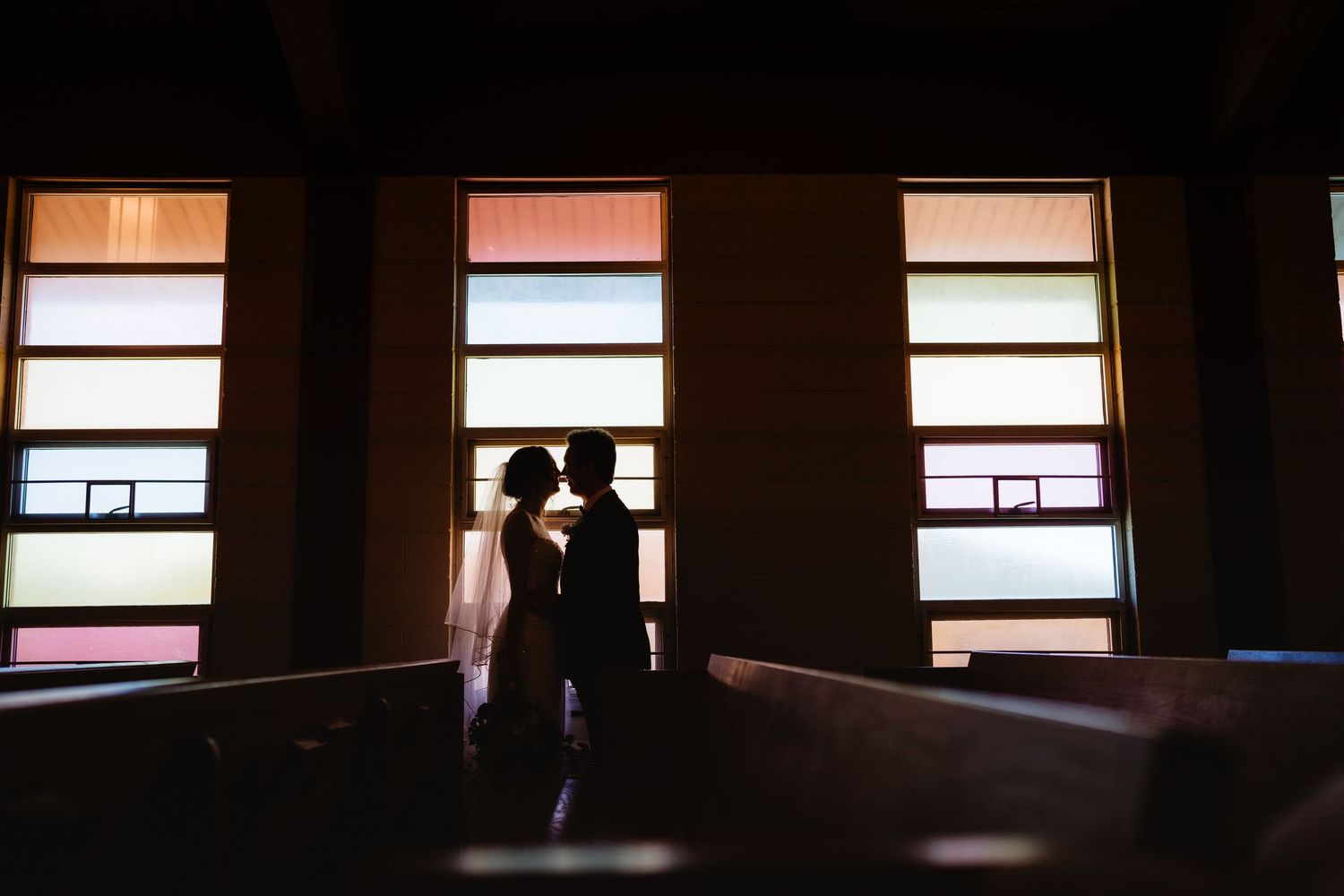 Silhouette of a couple sharing a romantic moment in a church with colorful stained glass windows behind them.