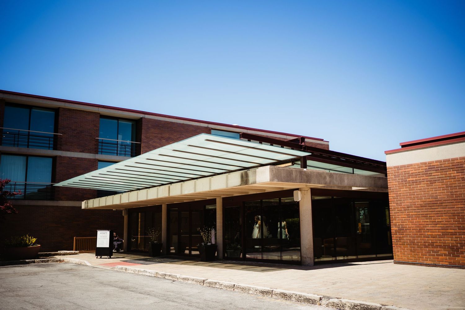 Brick building exterior with modern glass canopy entrance under clear blue sky.