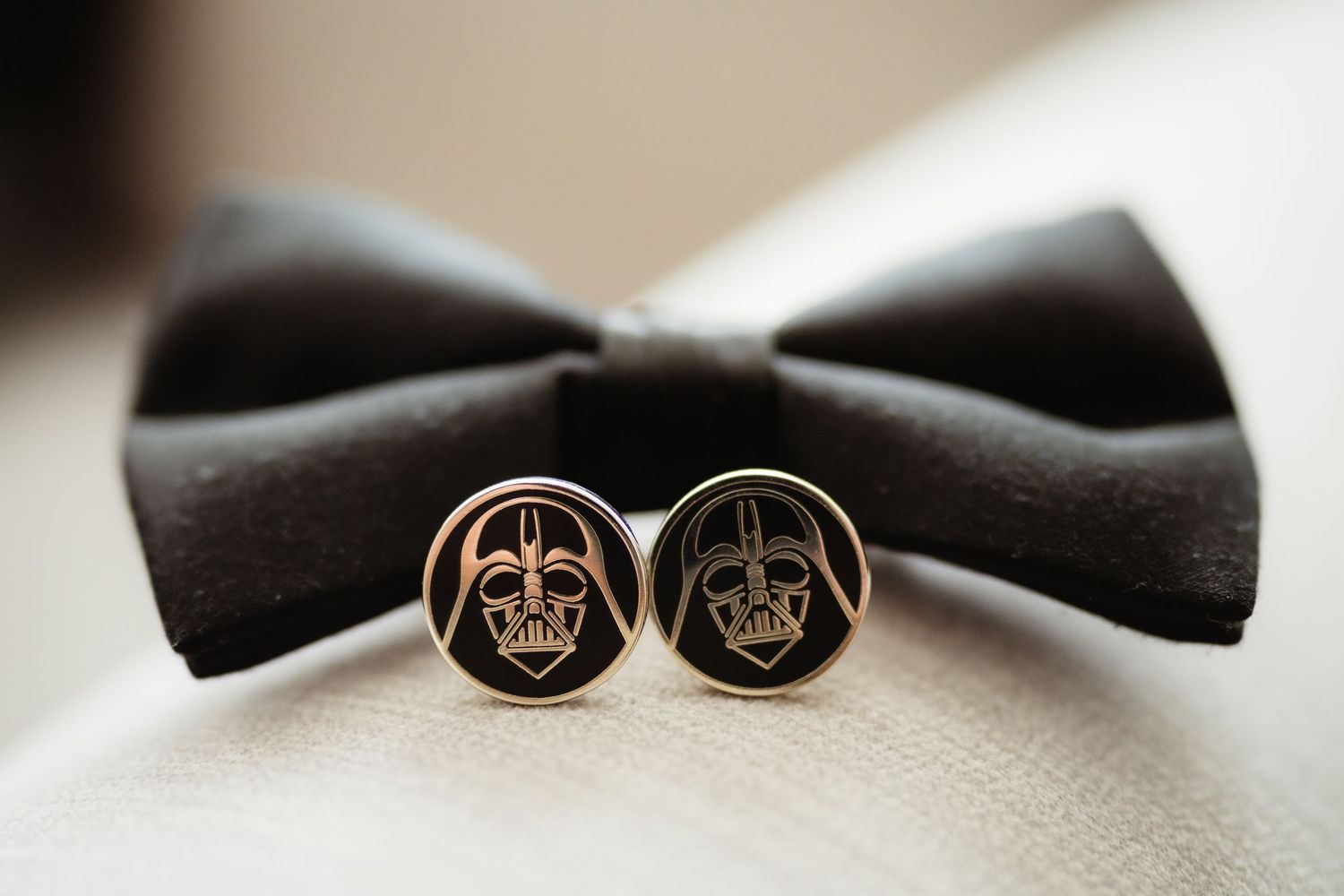 Darth Vader cufflinks resting in front of a black bow tie, perfect Star Wars wedding accessories for grooms.