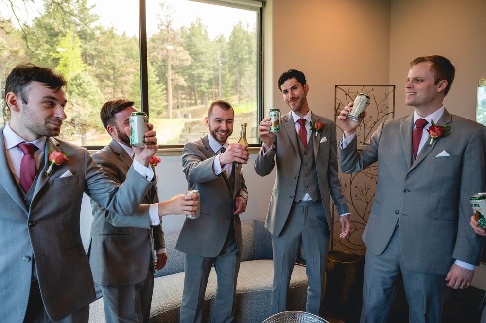 Groomsmen in gray suits toasting with drinks before a wedding ceremony.