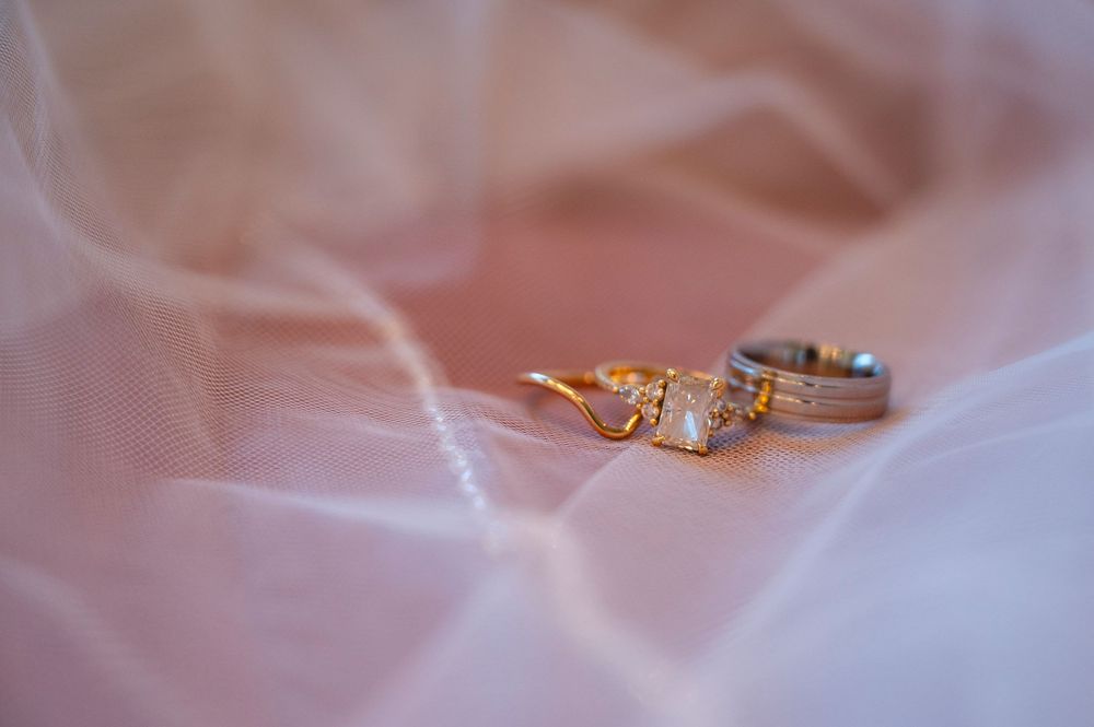 Gold diamond engagement ring and silver wedding band resting on soft pink bridal veil fabric.