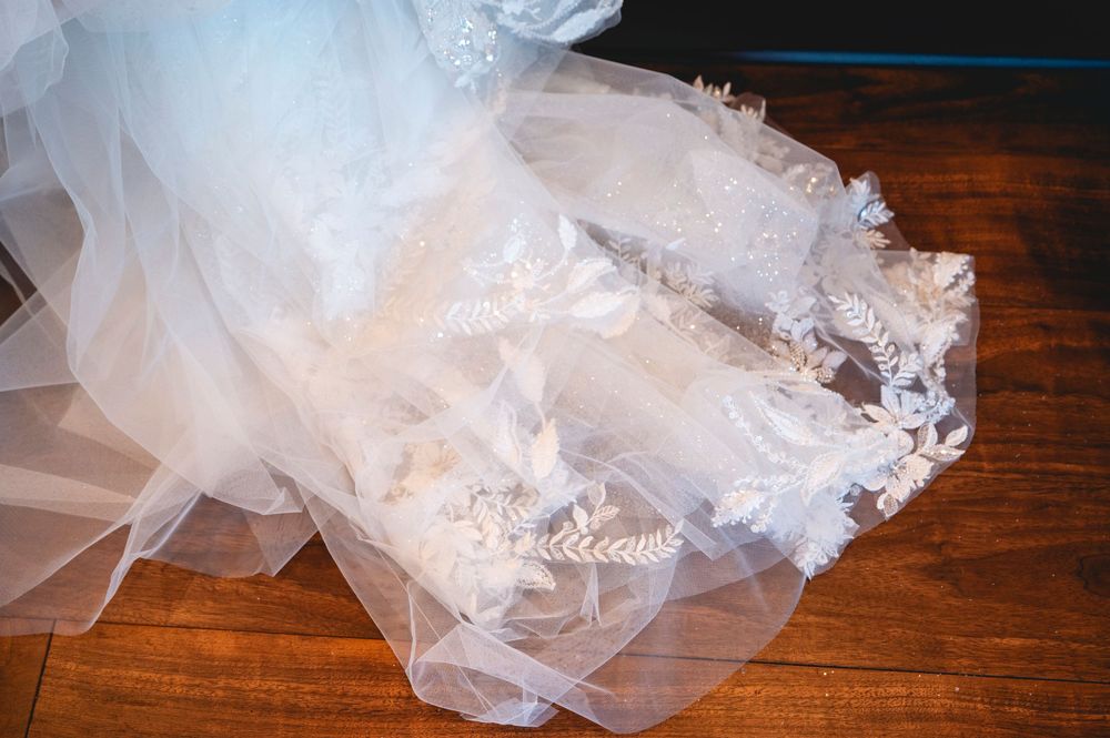 Elegant white wedding dress with intricate lace floral appliques and flowing tulle fabric spread on a wooden floor.